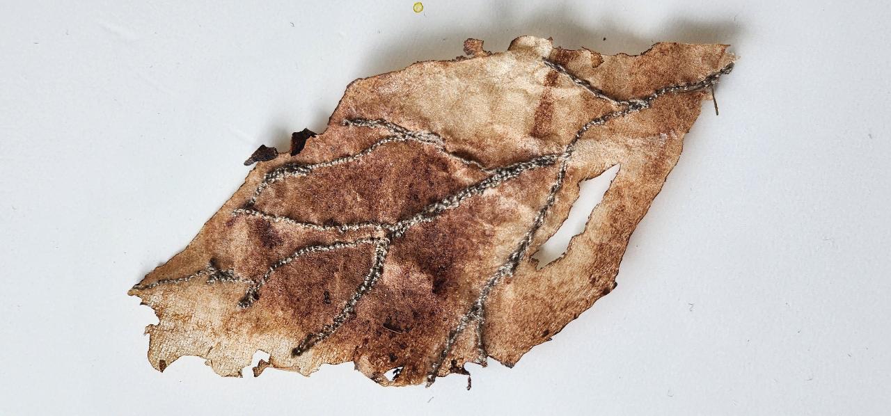 A stitched leaf artwork with decorative silver thread along its veins